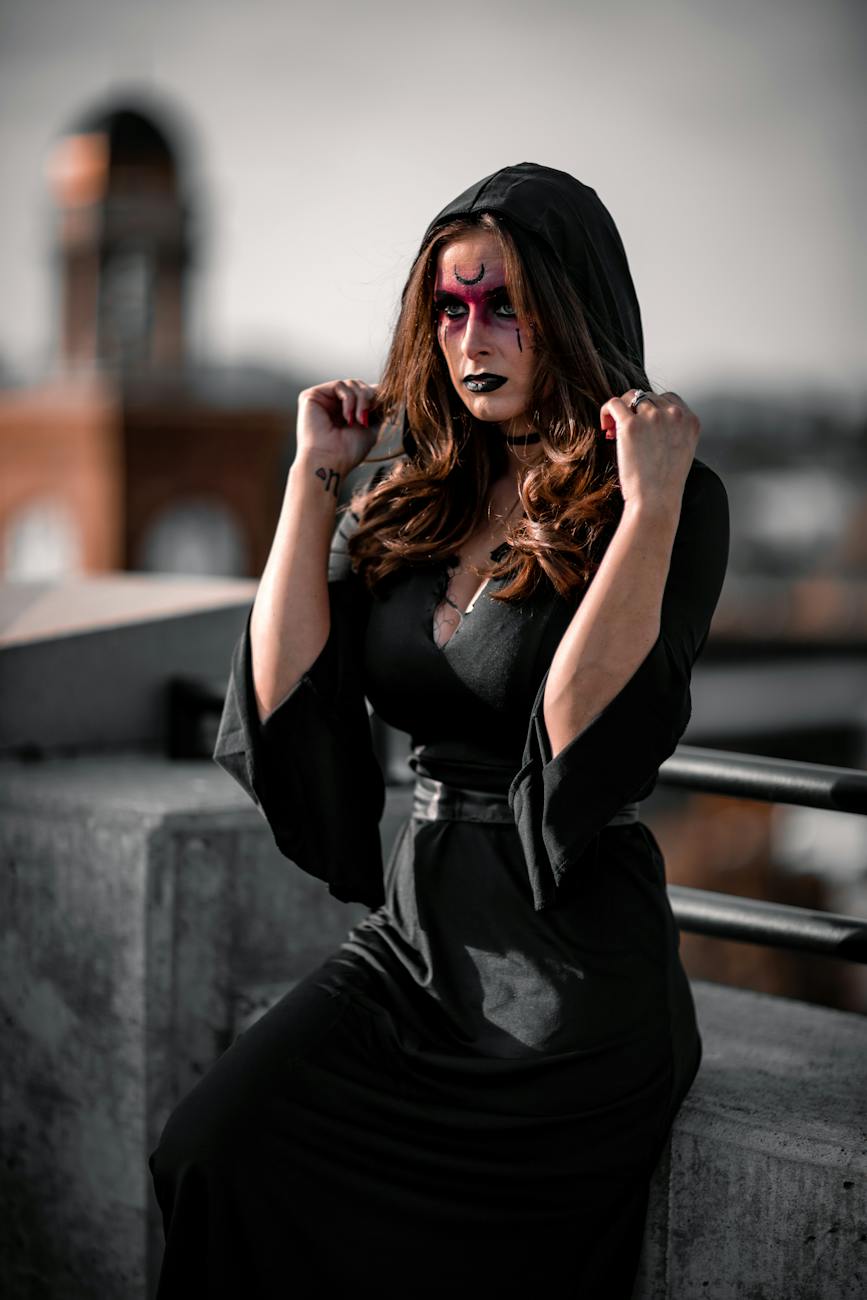 woman with painted face wearing black dress with a hood posing on a bridge